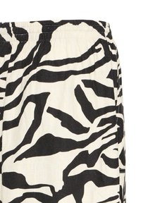 Tissu blanc avec un motif audacieux de rayures zébrées noires et une taille élastique, grosplan sur le détail d'un short ou d'un pantalon.