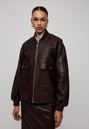 Giacca bomber in pelle bordeaux con una finitura texture, frontale con zip, ampie tasche e polsi a costine, abbinata a una gonna in pelle coordinata.