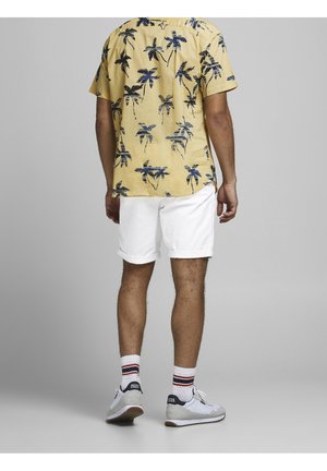 Gul kortærmet skjorte med sort og blå palme mønster, hvide shorts, grå sneakers med hvide accenter og stribede sokker.