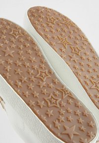 Suole di scarpe bianche con un motivo testurizzato di stelle di varie dimensioni su una base in gomma marrone chiaro e bordi scanalati visibili.