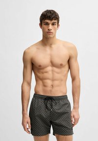 Costumi da bagno neri a fantasia con cintura regolabile, caratterizzati da una stampa a rombi e una texture liscia. Non vengono indossati altri indumenti.