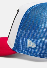 Gorra de béisbol roja y blanca con una sección de malla azul. Presenta un visor plano y un logo bordado en azul claro en el lado. Diseño de malla texturizada.