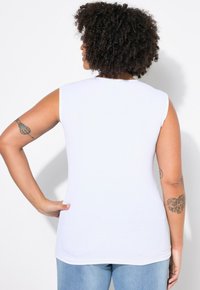 Top bianco senza maniche con texture a coste, scollatura tonda e design aderente, abbinato a jeans di denim blu chiaro.