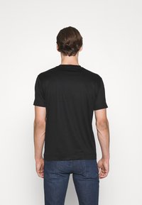 Svart t-shirt med kort ärm och rundad halsringning, mjuk textur och en figurnära passform, kombinerad med mörka jeans. Bakifrån visad.