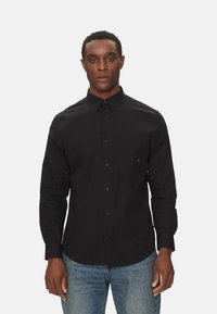 Camicia nera a maniche lunghe con bottoni, colletto, taschino frontale singolo e orlo dritto, abbinata a jeans blu.