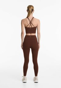 Sutien sport maro cu bretele încrucișate și colanți elastici înalți asortați, dintr-un material texturat, asortați cu încălțăminte sport ușoară.