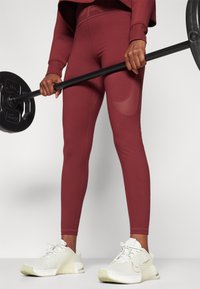 Leggings bordo cu un design ajustat și accente din plasă, asortate cu adidași albi cu o suprafață texturată și detalii verzi.