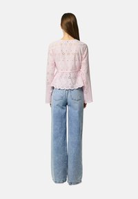 Lys pink, bluse med eyelet-mønster og lange ærmer, peplum-talje og bølget kant, kombineret med højhalsede blå jeans.