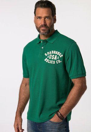 Grøn polo-skorte med klassisk krave, prydet med hvid tekst "Roadhouse USA Relics Co." på brystet; lavet af bomuld, korte ærmer.
