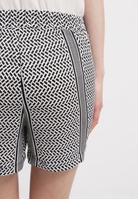 Černobílé šortky s elastickým pasem, které mají geometrický vzor a boční akcenty v kontrastní barvě.