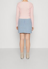 Haut à manches longues côtelé rose clair avec détail de bouton au dos, associé à une mini-jupe bleue à motif pied-de-poule. Le modèle porte des bottines à talons beiges.
