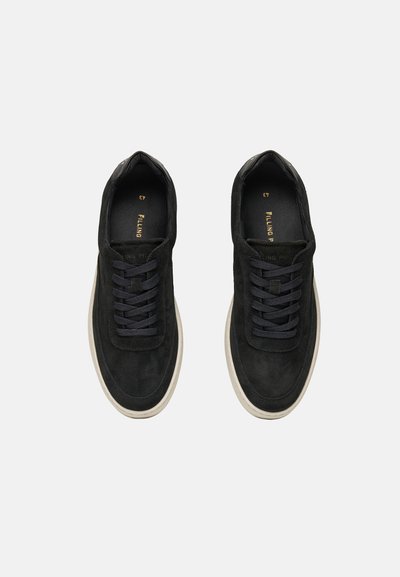 Par sorte ruskind snørebåndssneakers med hvide såler set fra oven på en ensfarvet baggrund.