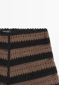 Close-up van bruin en zwart gehaakte stof met horizontale strepen en een Massimo Dutti-label aan de bovenrand.