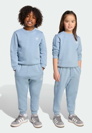 Sweatshirt et joggings bleu clair en tissu doux, avec des poignets côtelés et un petit logo blanc sur la poitrine et la jambe du pantalon.
