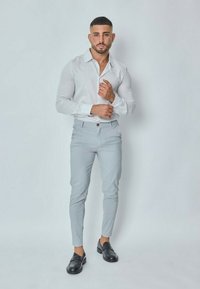 Chemise blanche à rayures, pantalon taillé gris clair, mocassins noirs ; tissu lisse, coupe ajustée, ourlet arrondi et détails minimalistes.