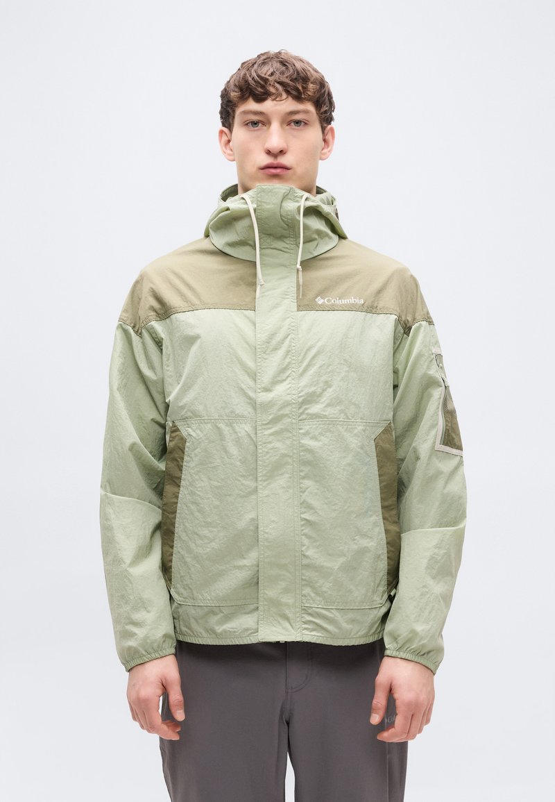 Ανοιχτό πράσινο μπουφάν με κουκούλα, με σκούρες πράσινες λεπτομέρειες, ελαστικές μανσέτες και φερμουάρ μπροστά. Κατασκευασμένο από ελαφρύ, υφή ύφασμα.