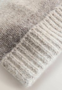 Light gray and beige knitted wool sweater detail, featuring a ribbed hem and a soft, textured finish transitioning from light to dark.