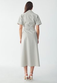 Light grey shirt dress with short sleeves, belted waist, and a long, flowing skirt. Smooth texture and simple design. White high-heeled sandals.
