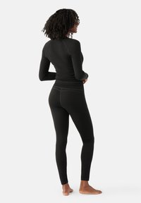 Svart långärmad topp och figurnära leggings, tillverkade av slät, elastisk tyg, med kontrasterande sömnadsdetaljer och en sömlös design.