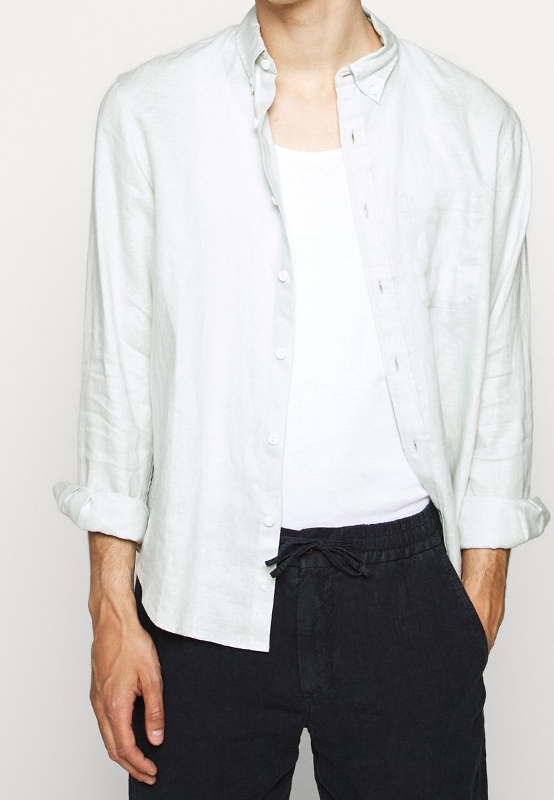 Ljusgrön linneskjorta med knäppbar krage, långärmad som är uppvikt. I kombination med svarta byxor med dragsko och vit undertröja.