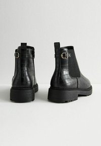 Botines de cuero negro con estampado de cocodrilo, paneles laterales elásticos texturizados, un acento de hebilla y suelas de goma gruesas.