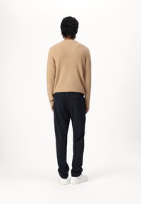 Beige våffelstickad tröja, mörka randiga byxor, vita sneakers; sedd bakifrån, avslappnad och ledig passform.