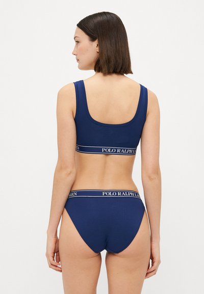 Tamsiai mėlynas braletė ir suderinti apatiniai, pagaminti iš minkštos medžiagos. Viršus turi platų, ženklais pažymėtą diržą su "POLO RALPH LAUREN" užrašu apatinėje dalyje.