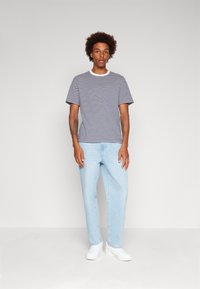 T-shirt rayé en bleu marine et blanc, à manches courtes, col rond côtelé, associé à un jean décontracté bleu clair et des baskets blanches.