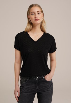 Maglietta nera a maniche corte con scollatura a V, caratterizzata da un motivo a zigzag testurizzato, maniche leggermente arrotolate e una vestibilità rilassata, abbinata a jeans scuri.