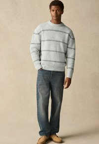 Gray striped sweater in a textured knit, paired with loose-fitting blue denim jeans and beige shoes, set against a neutral background.