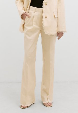 Beige op maat gemaakte suit met rafelige randen, slim fit broek en een losse blazer. Beide hebben een gladde textuur en een minimalistisch ontwerp.