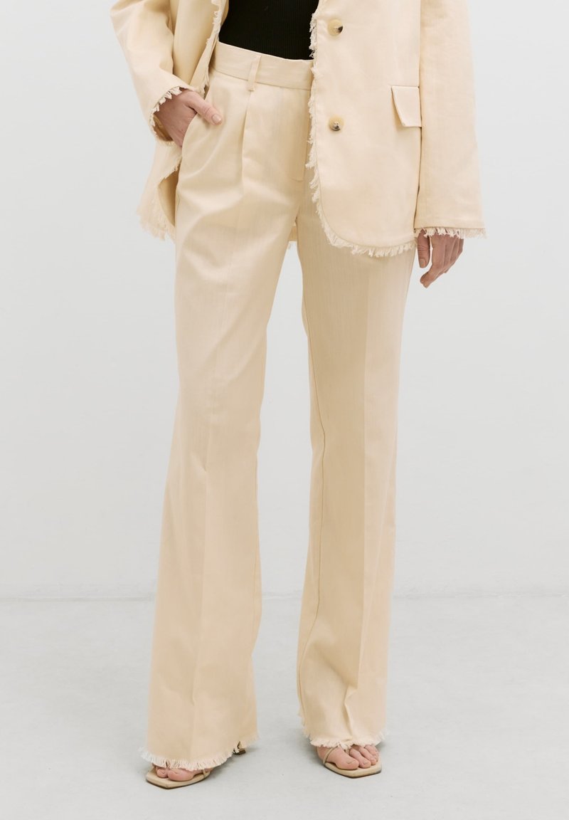 Beige op maat gemaakte suit met rafelige randen, slim fit broek en een losse blazer. Beide hebben een gladde textuur en een minimalistisch ontwerp.