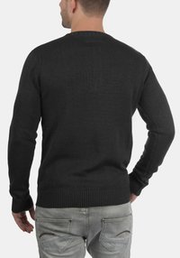 Maglione nero a maglia con scollo rotondo e polsini a coste. Presenta una finitura testurizzata e una vestibilità rilassata, abbinato a jeans grigi chiari.