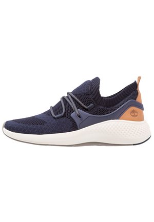 Marineblå strikket sneaker med hvid sål, elastiske snørebånd og brun læderhæl med prægede træ-logo.