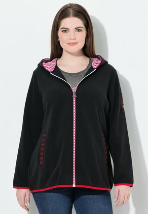 Veste en polaire noire avec une doublure de capuche à carreaux rouge et blanc, zip contrastant, poches latérales avec des accents décoratifs, et une coupe décontractée.