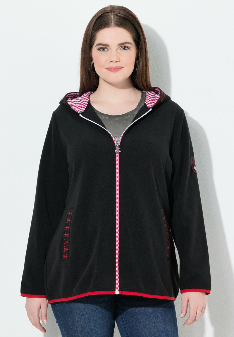 Veste en polaire noire avec une doublure de capuche à carreaux rouge et blanc, zip contrastant, poches latérales avec des accents décoratifs, et une coupe décontractée.