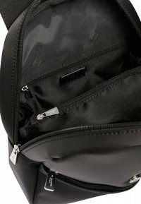 Zaino nero realizzato in un tessuto liscio, dotato di numerosi scomparti con zip e accessori in metallo argentato, con un motivo interno sottile.