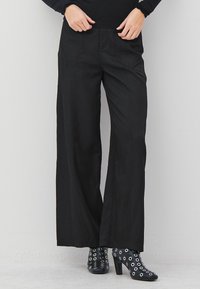 Črne široke hlače s sprednjimi šivi, oblečene z visokimi črnimi čevlji na peto, ki imajo okrogle srebrne očesce.