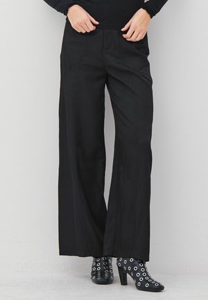 Svarta vida byxor med framsydda detaljer som bärs med svarta högklackade ankelstövlar med runda silveröglor.