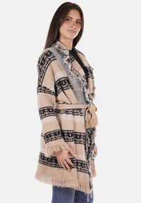 Cardigan a fantasia beige e nera con frange, realizzato in tessuto morbido. Presenta una cintura e un colletto a scialle, progettato per comfort e calore.