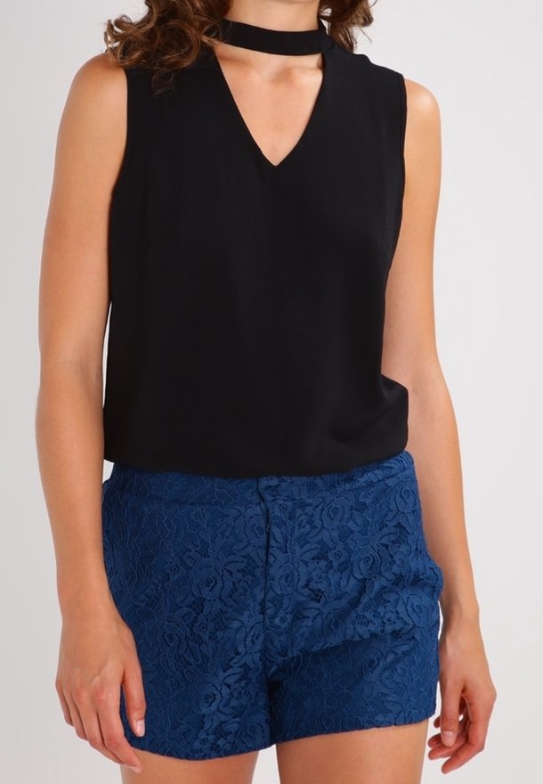 Schwarzes ärmelloses Top mit V-Ausschnitt und Choker-Detail, kombiniert mit strukturierten dunkelblauen Spitzen-Shorts mit floralem Muster.