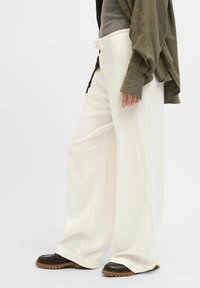 Pantalons larges blancs en tissu doux avec une taille à cordon, associés à des chaussures marron foncé avec une semelle texturée.