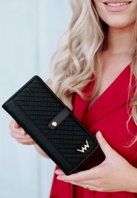 Black wallet made of textured material, featuring a quilted pattern, gold hardware accents, and a snap closure.