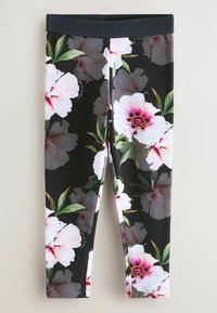 Leggings floraux avec une base noire présentant de grands motifs de fleurs roses et blanches. Tissu lisse et extensible avec une large ceinture.