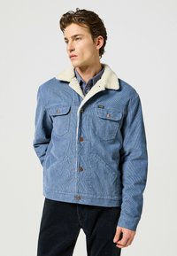 Blå kordjacka med en krämfärgad faux shearling-krage, två bröstfickor och knäppning framtill, med en texturerad yta.