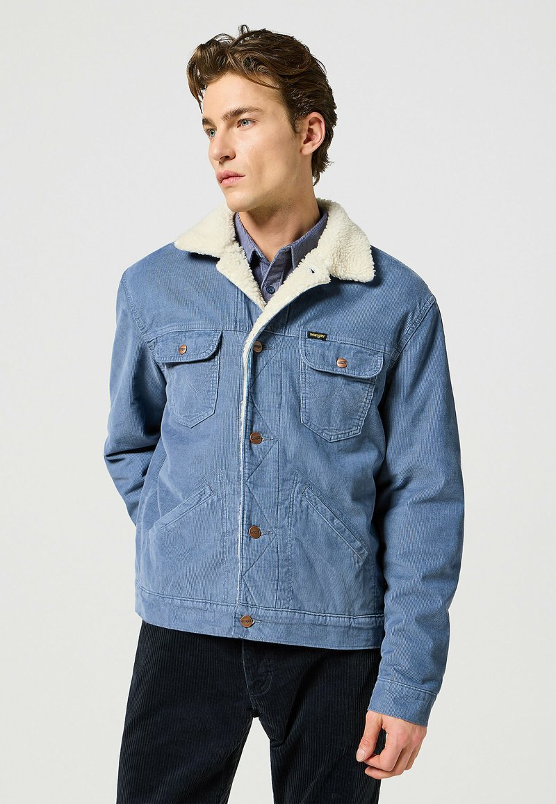 Blå kordjacka med en krämfärgad faux shearling-krage, två bröstfickor och knäppning framtill, med en texturerad yta.