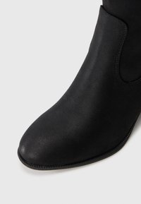 Black ankle boot made of smooth material, featuring a pointed toe, simple design, with minimal stitching detail along the sole.