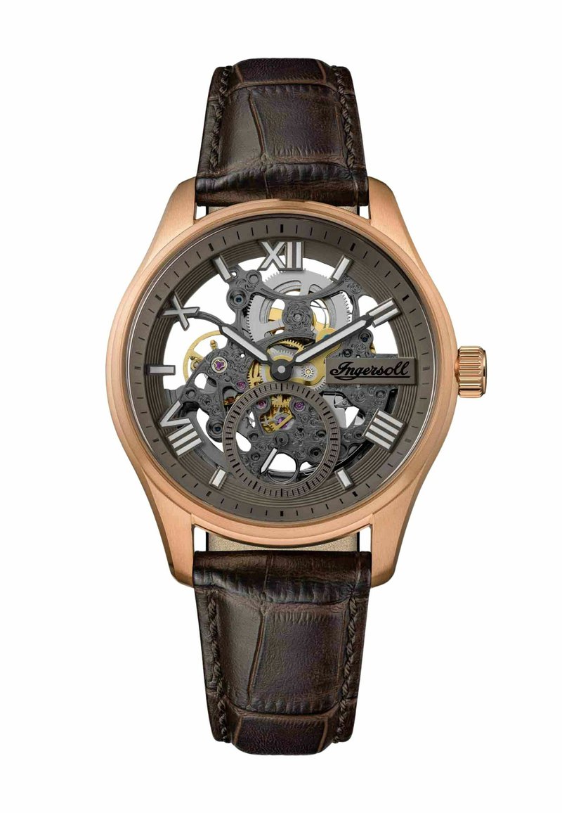 Montre squelette avec un boîtier en bronze, cadran gris et mouvement exposé. Le bracelet en cuir brun présente une finition texturée. Chiffres romains aux positions 12 et 6.