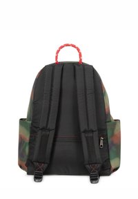 Zaino con motivo camouflage in verde e marrone, corpo in tessuto nero, spallacci imbottiti e maniglia superiore rossa con accenti bianchi.