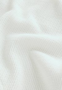 Tissu blanc doux avec une texture subtile en nid d'abeille et de légères plis créant une apparence délicatement froissée.